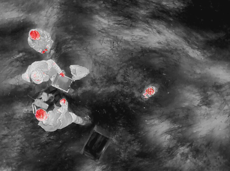 Image thermique de trois personnes et d’un petit animal sur le terrain, mis en évidence par des signatures thermiques rouges.