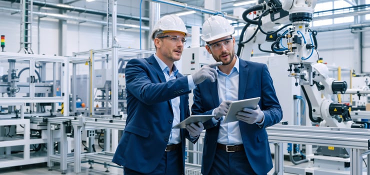 2 hommes portant un casque et des lunettes de protection dans un environnement de production robotisé.