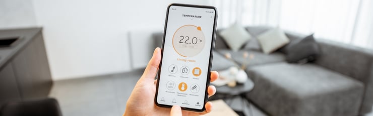 Une personne tient un smartphone affichant une application domotique pour régler la température dans un salon moderne.