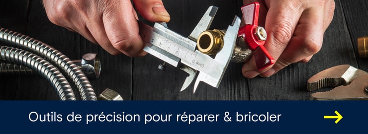 Pied à coulisse mesurant avec précision un raccord en laiton à côté d’outils et de conduites métalliques flexibles