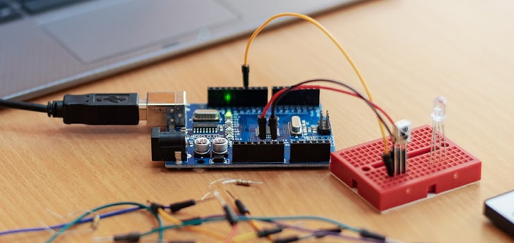 Carte de développement Arduino sur un bureau, connectée via USB et reliée par des câbles à une carte d'expérimentation rouge avec LED.