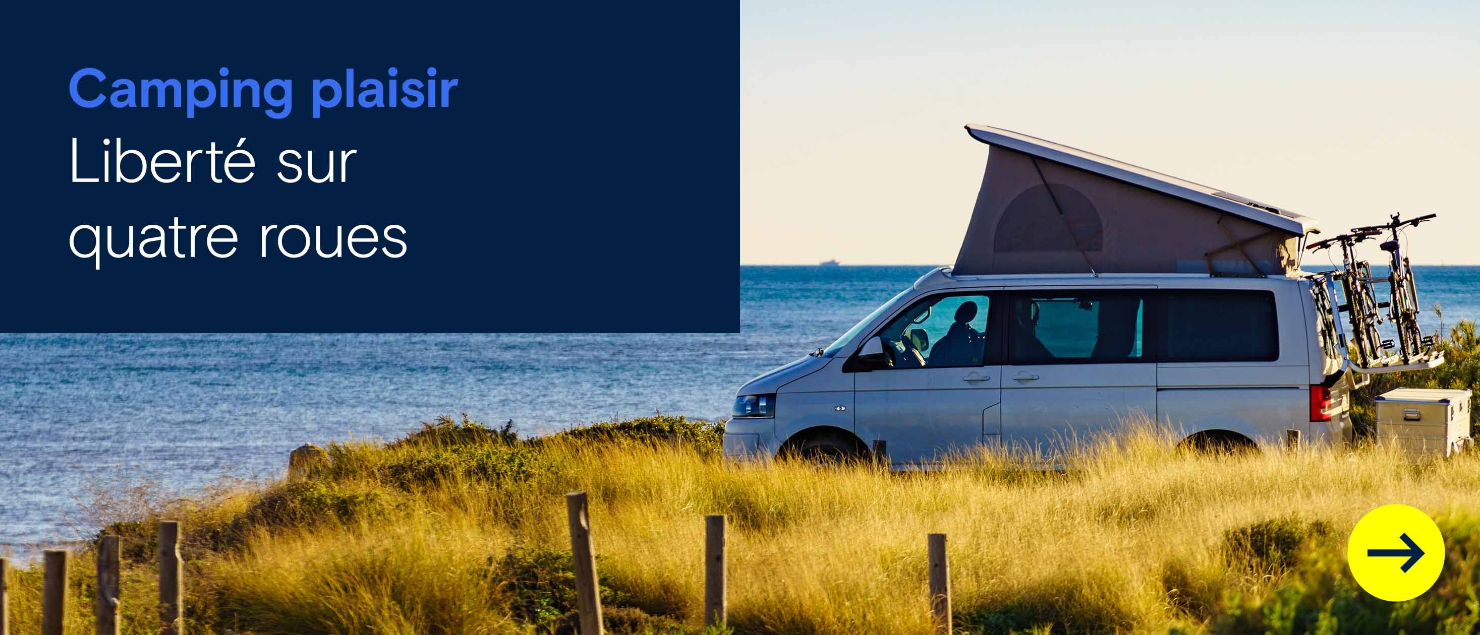 Un van de camping avec le toit relevé est garé face à la mer, l’horizon en arrière-plan.