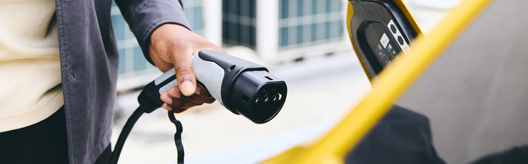 Une personne tient un câble de recharge à brancher à une voiture électrique.