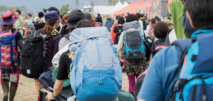 Un groupe de personnes avec de grands sacs à dos marche sur un terrain de festival ou de camping.