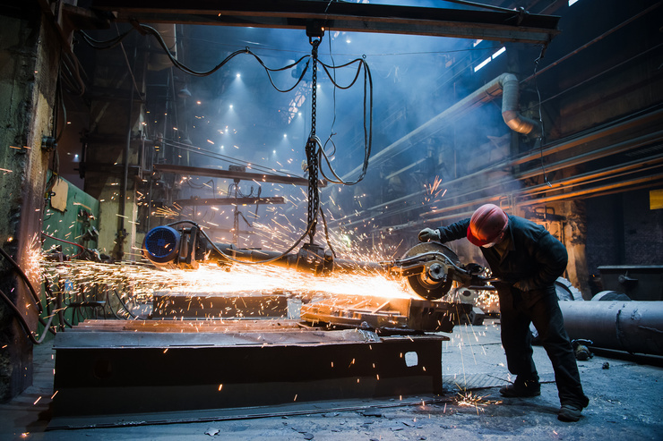Un ouvrier coupe du métal avec une scie électrique dans une usine, des étincelles volent autour de lui.