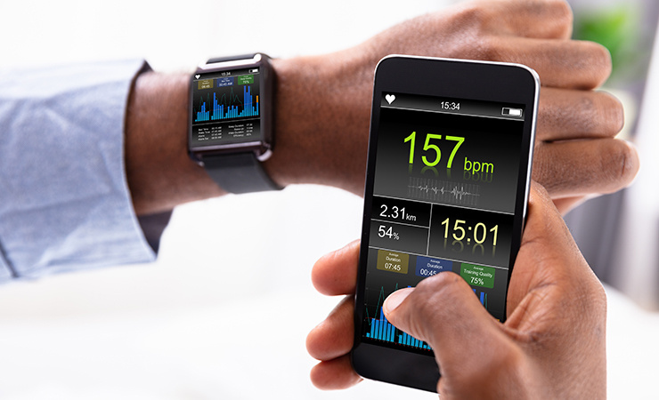 Une personne tient dans sa main un smartphone contenant des données relatives à sa condition physique et porte au poignet une montre connectée affichant son niveau d'activité.
