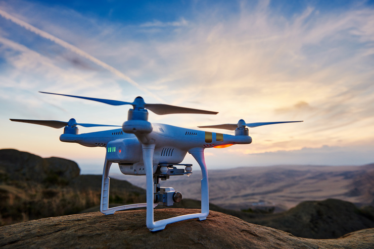 Un drone se tient sur une roche devant un paysage au coucher du soleil.