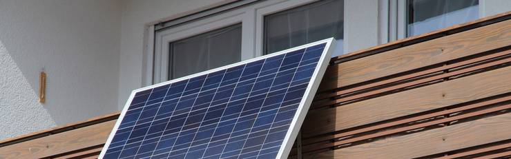 Un module solaire est fixé sur un balcon devant une fenêtre et orienté vers le soleil.