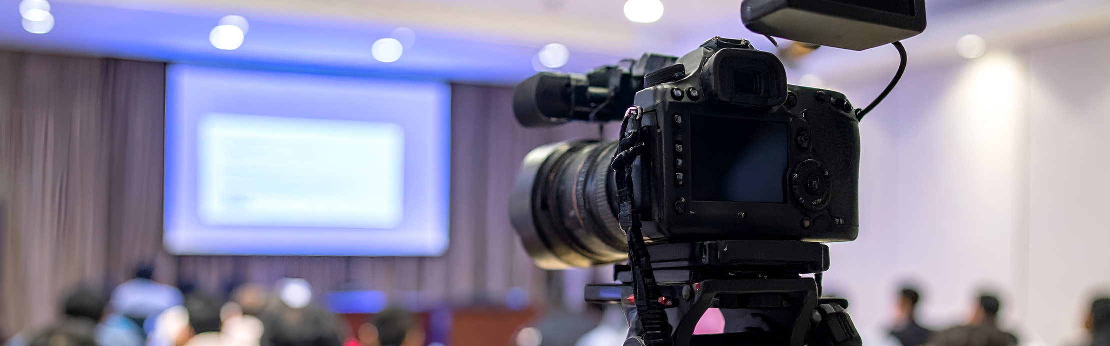 Une caméra vidéo montée sur un trépied filme une présentation dans une salle de conférence