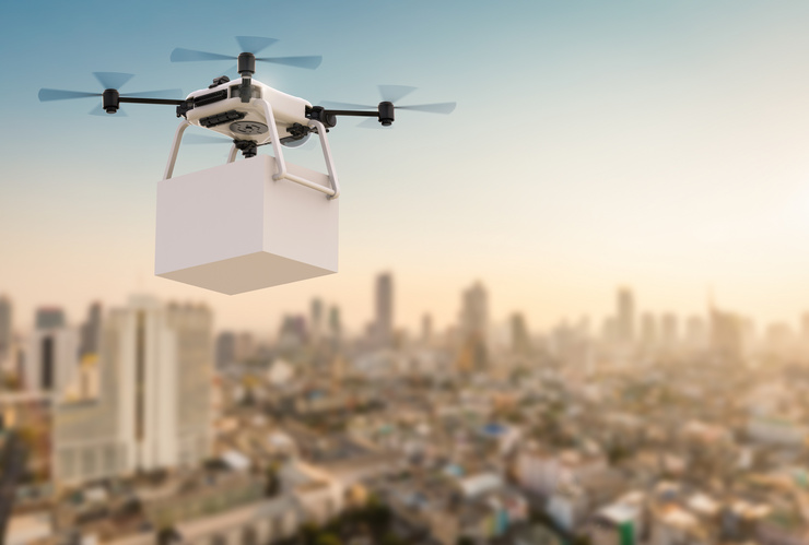 Drone avec un colis en vol au-dessus d'une ville au coucher du soleil.