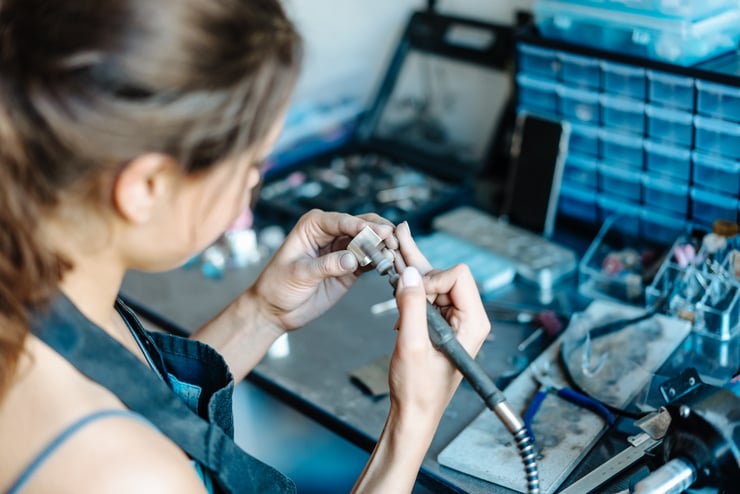 Une femme travaille avec un microscope dans un environnement d'atelier ou de laboratoire.