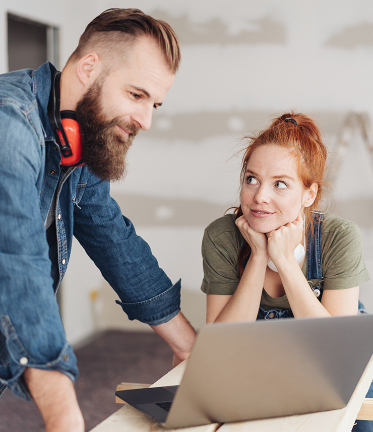 Un homme et une femme planifient ensemble sur un ordinateur portable dans une pièce en cours de rénovation