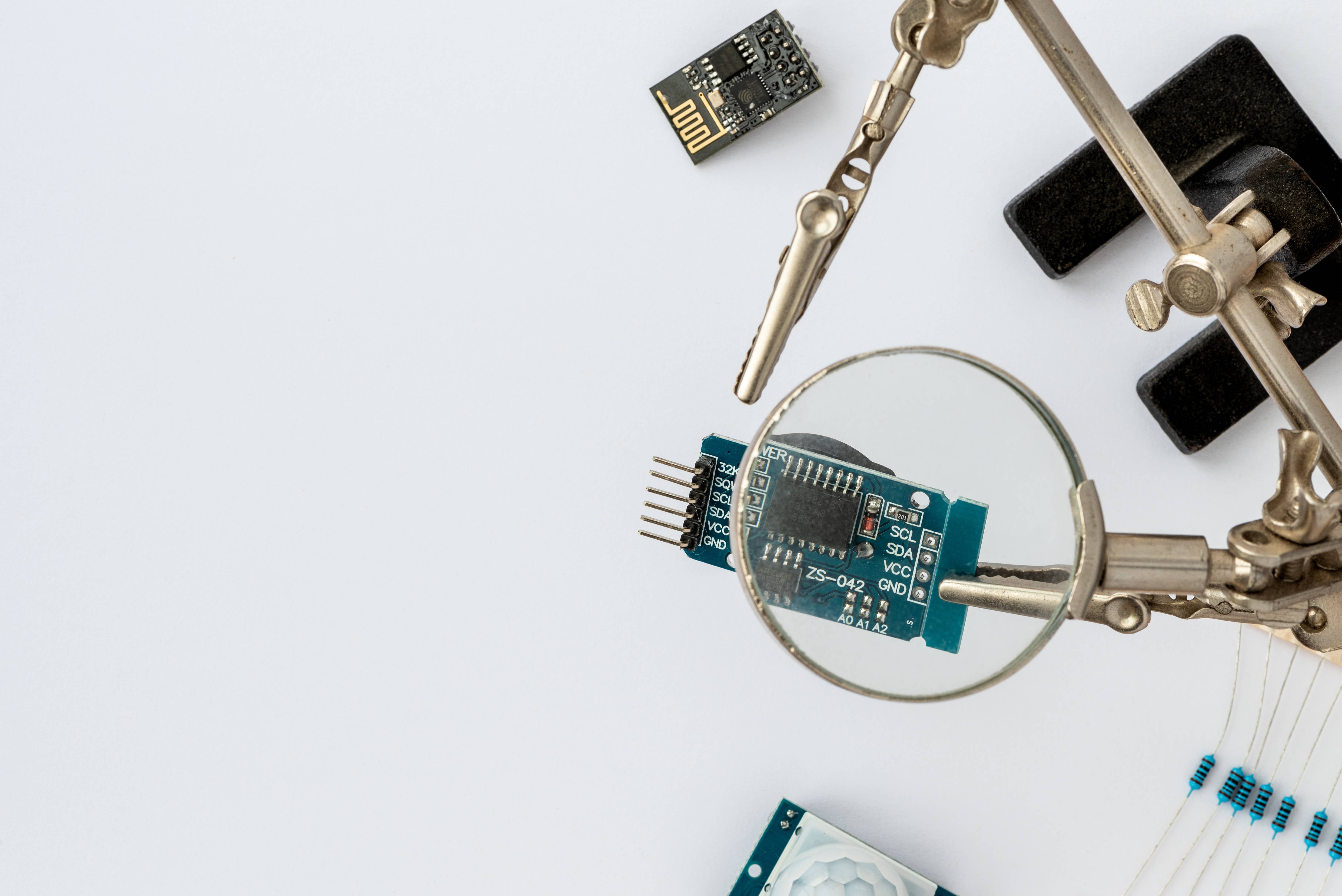 Gros plan d'un microcontrôleur bleu tenu avec une loupe, entouré d'une clé USB, d'un tournevis et d'un composant électronique.