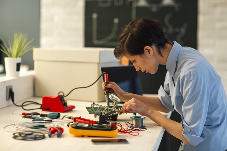 Une femme travaille sur un appareil électronique avec des outils sur une table.