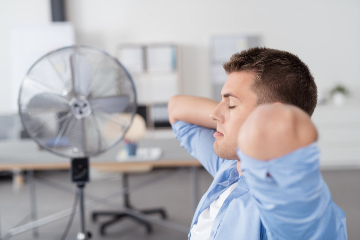 Un ouvrier assis devant un ventilateur dans une pièce surchauffée