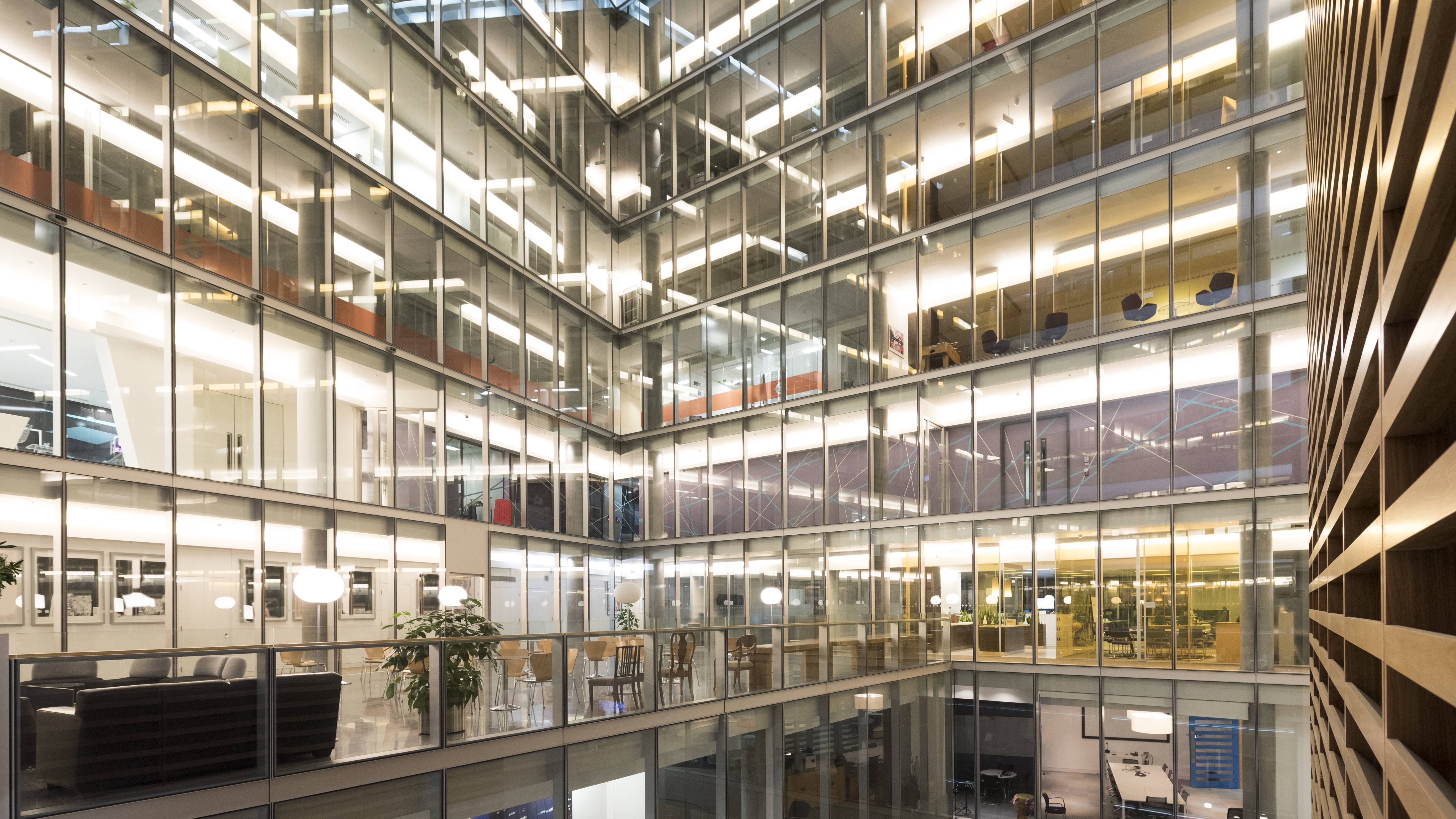 Vue d'un bâtiment de bureaux moderne à plusieurs étages avec de grandes façades en verre et des espaces de travail visibles.