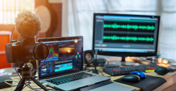 Une personne parle dans un micro professionnel devant un ordinateur portable, elle porte un casque et des lunettes.