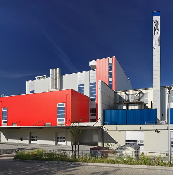 L'usine Knipex, avec ses façades modernes rouges et blanches. Une silhouette de pince est dessinée sur la haute cheminée blanche.