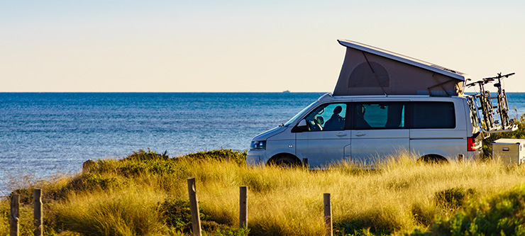 Un van de camping avec le toit relevé est garé face à la mer, l’horizon en arrière-plan.