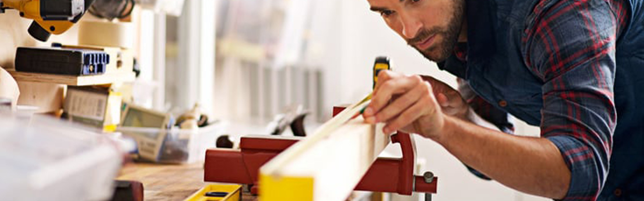 Une personne utilise un niveau à bulle pour mesurer une pièce fixée sur un établi, dans un atelier bien équipé destiné aux travaux de bricolage et de montage de précision.