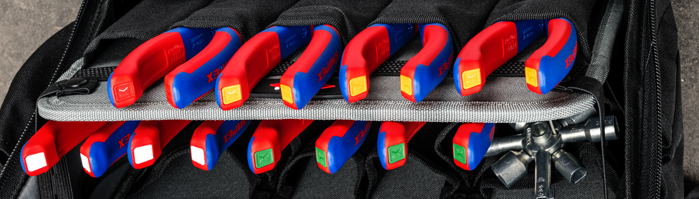 Un gros plan d'une sacoche à outils, remplie de deux rangées de pinces Knipex avec des poignées isolées rouge et bleu.