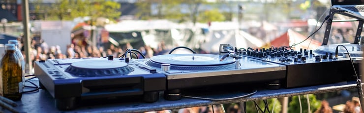 Matériel de DJ sur une scène de festival avec un public flouté en arrière-plan.