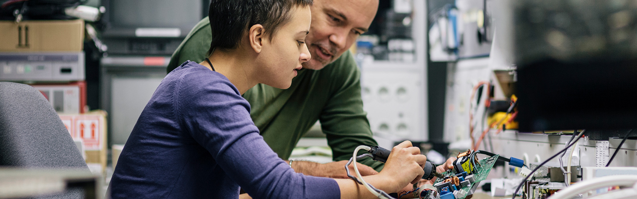 Un homme âgé explique simplement une technique de brasage à un jeune. 