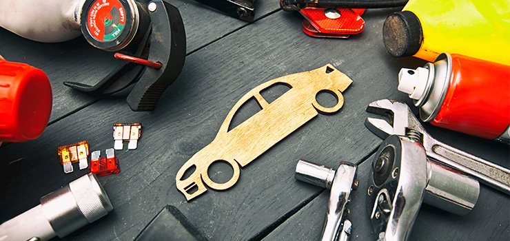 Divers outils et accessoires automobiles sont posés sur un établi à côté d’une forme de voiture en bois.