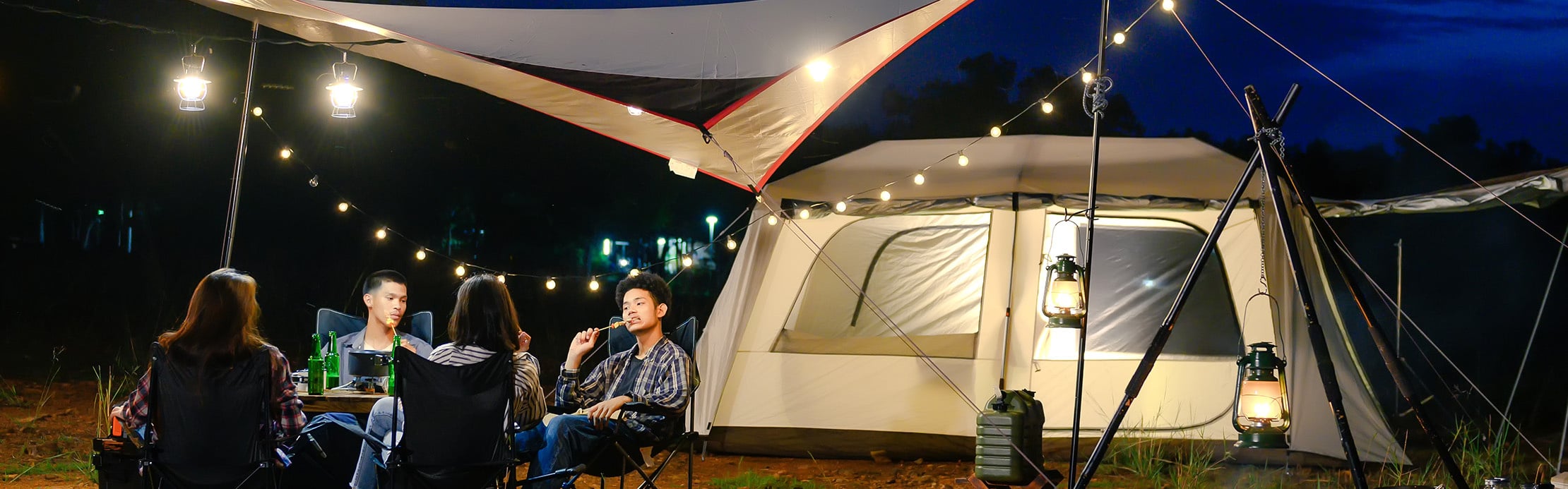 Un groupe de personnes est assis le soir devant une tente éclairée dans un camping et profite de ce moment passé ensemble en plein air.
