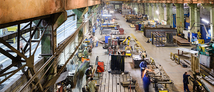 Vue grand angle d’un grand hall industriel avec de nombreux postes de travail et des personnes.