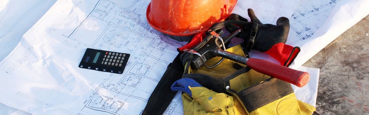 Outils, casque de sécurité et calculatrice posés sur des plans pour la planification de chantier.