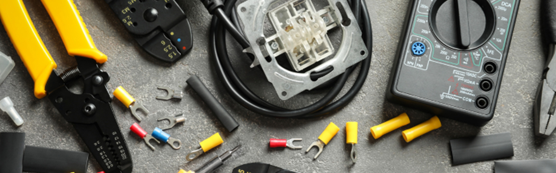 Divers outils et composants électriques, notamment des pinces, des câbles, un appareil de mesure et un connecteur, répartis sur une surface grise.