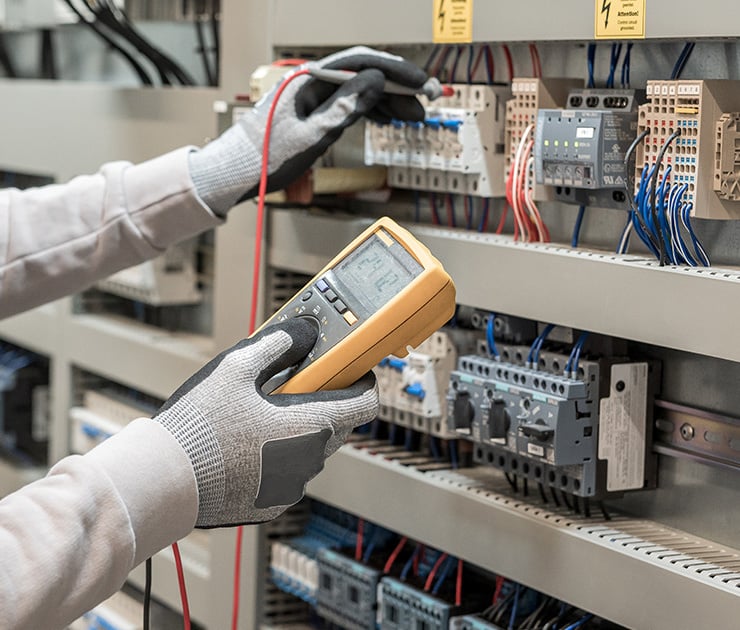 Un technicien mesure les paramètres électriques dans une armoire électrique à l'aide d'un multimètre.