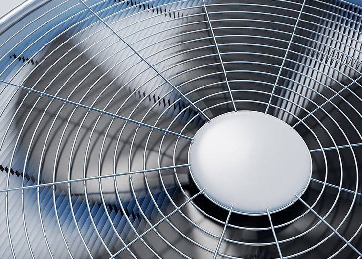 Gros plan sur un ventilateur en marche avec des pales de rotor argentées derrière une grille de protection.