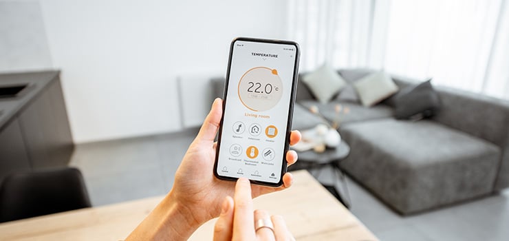 Une personne tient un smartphone affichant une application domotique pour régler la température dans un salon moderne.