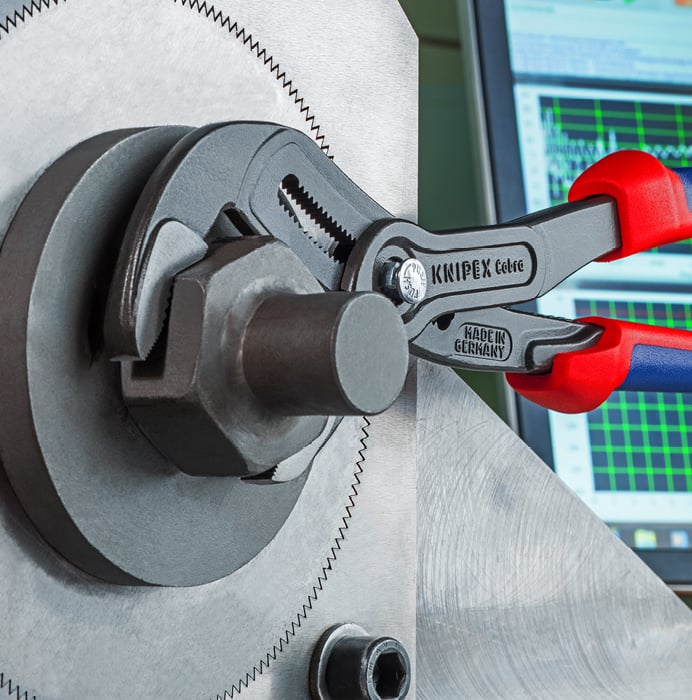 Une pince-multiprise Knipex Cobra en action sur un grand écrou hexagonal, avec des graphiques sur un écran en arrière-plan.