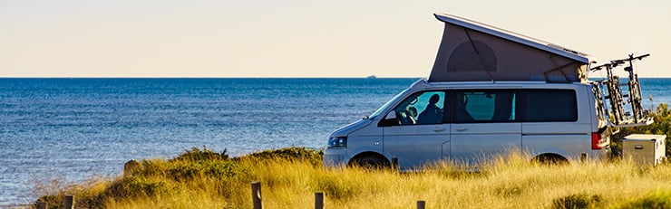 Un camping-car avec toit relevable ouvert est garé sur une côte avec vue sur la mer.