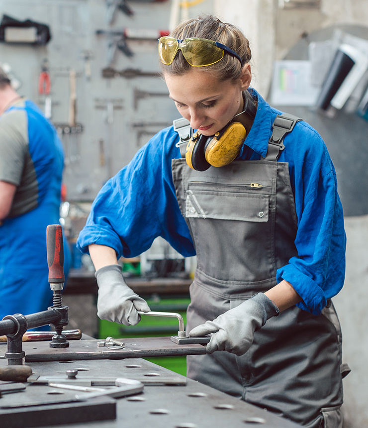 Un spécialiste équipé de lunettes de protection et d'une protection auditive assemble un composant métallique à l'aide d'un outil dans un atelier.