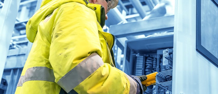 Technicien en tenue de protection travaillant avec un appareil de mesure sur une armoire électrique ouverte dans un hôpital