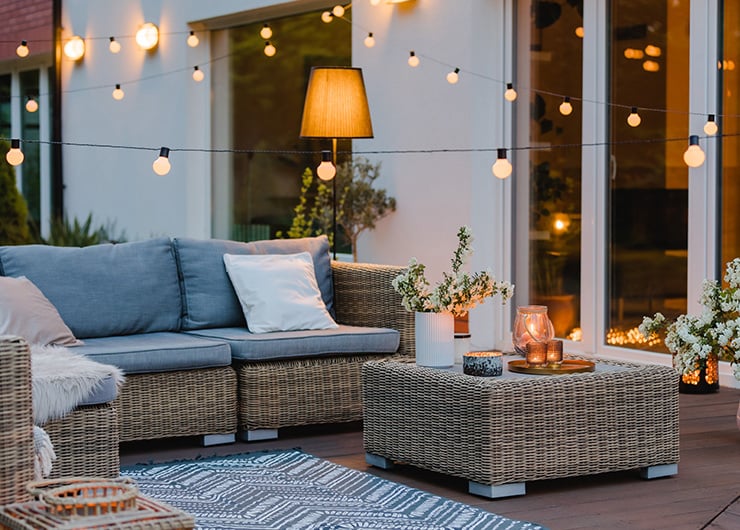 Une terrasse confortable avec des meubles de salon, une guirlande lumineuse et une lumière chaleureuse pour créer une ambiance agréable en soirée.