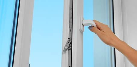 Hand öffnet weißes Fenster, blauer Himmel im Hintergrund. Weiterleitung zum Ratgeber zur Raumluft