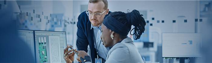 Man en vrouw kijken naar twee computerschermen, kantooromgeving. Ontdek nu SourcingPlus.